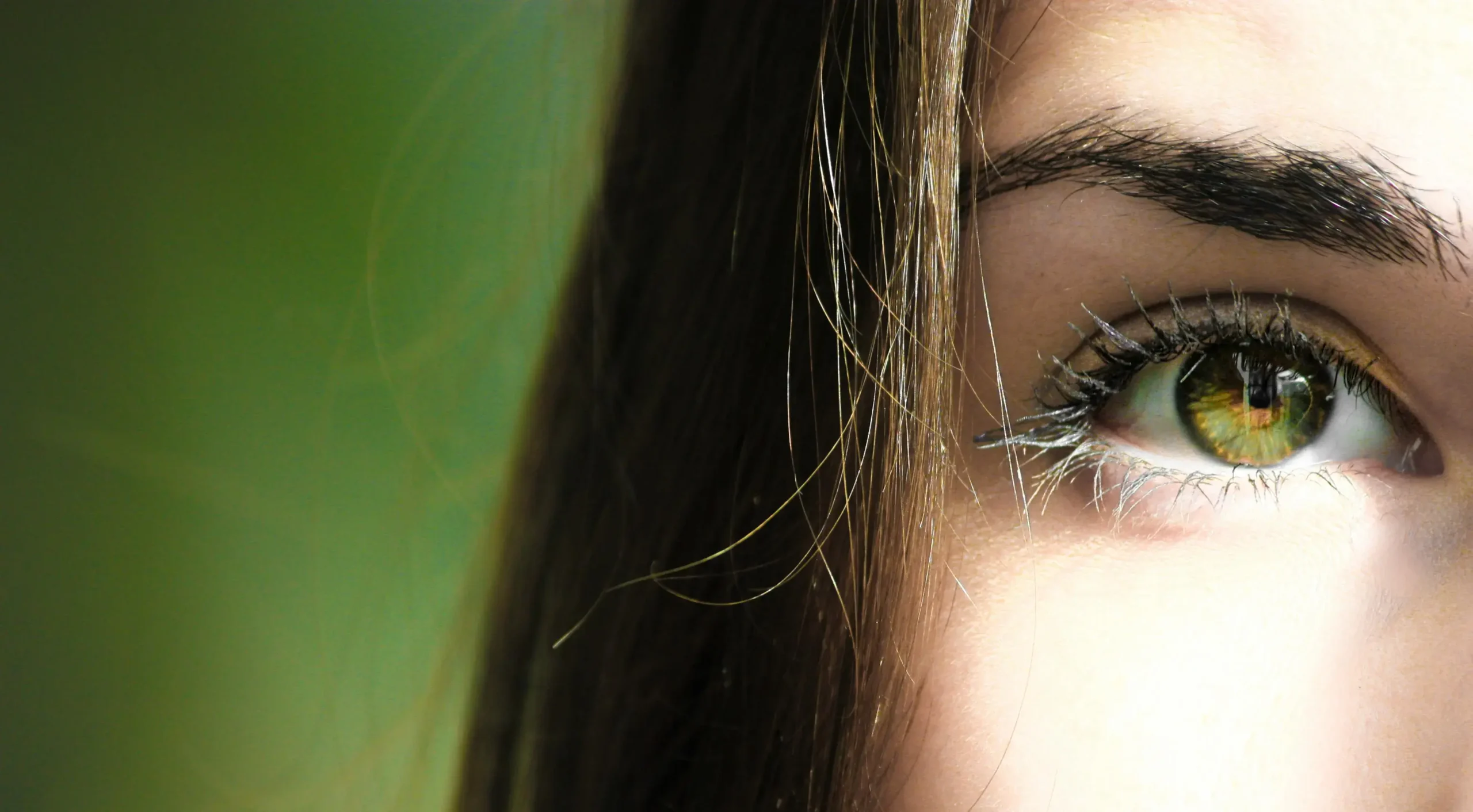 Close-up of a woman's eye showcasing a vibrant green iris and delicate eyelashes.